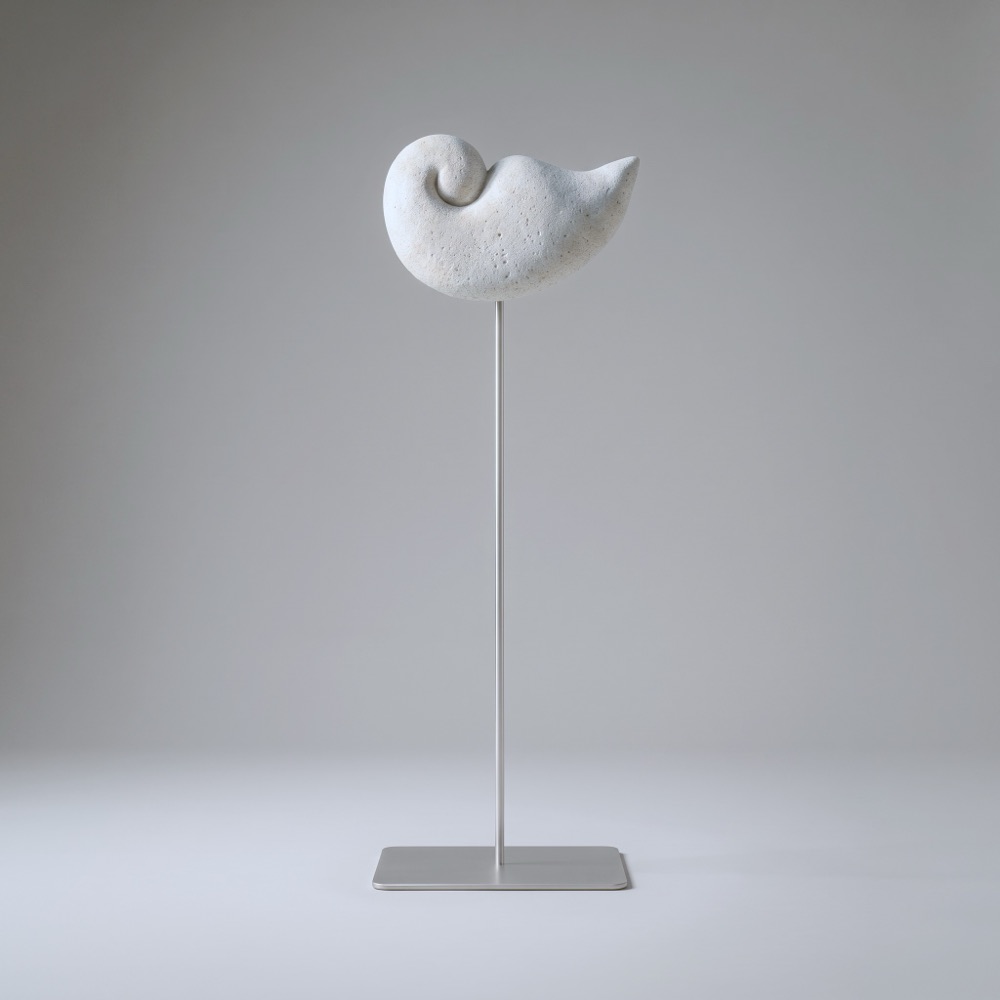 A small curled form, like a sleeping bird, carved in aerated concrete and held high on a thin stainless-steel rod.